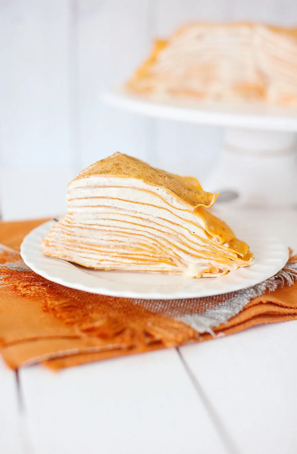 Pumpkin spice crepe cake on a white plate with an orange napkin. 