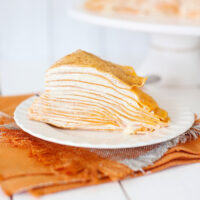 Pumpkin spice crepe cake on a white plate with an orange napkin.