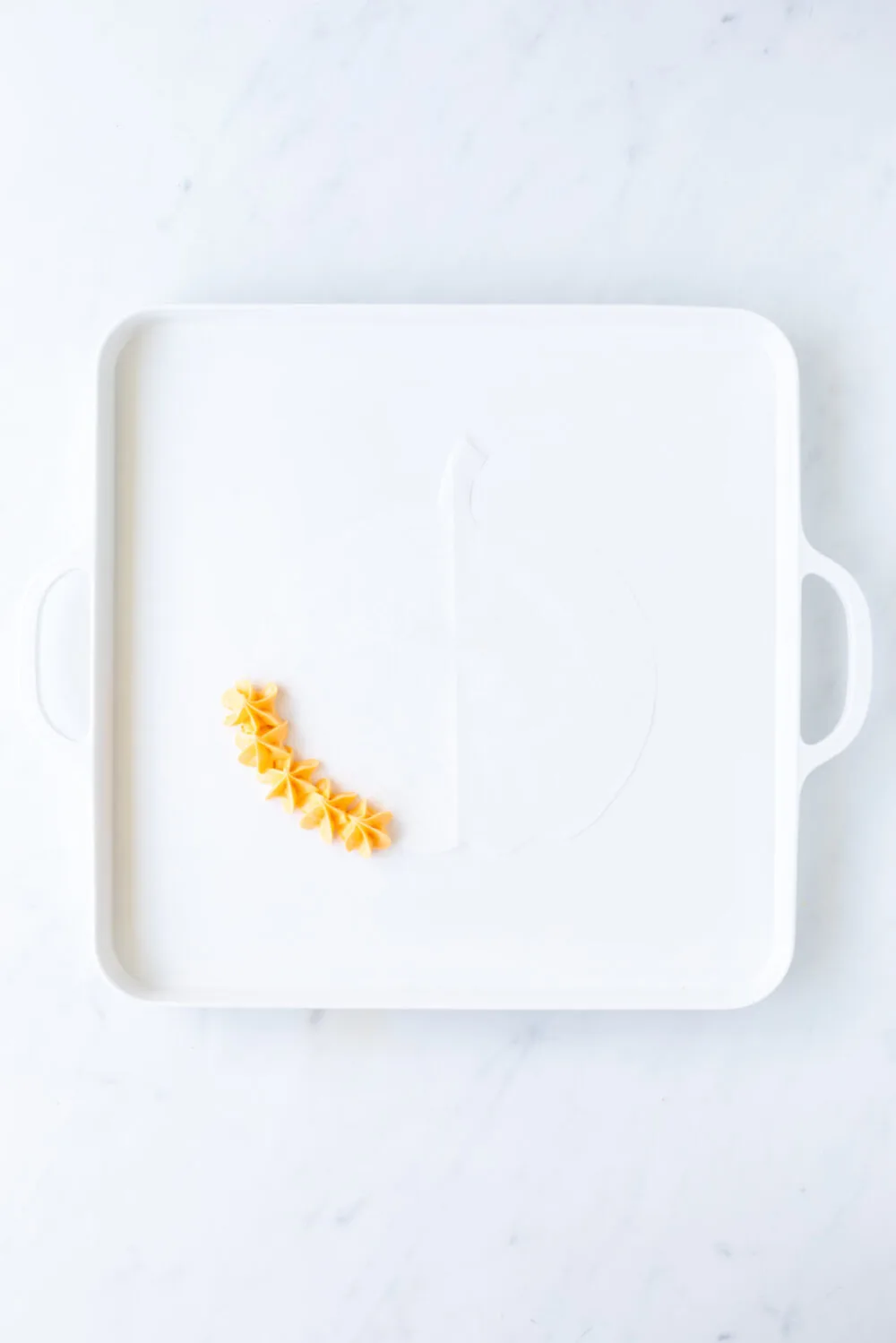 Adding orange frosting to parchment paper on a board. 