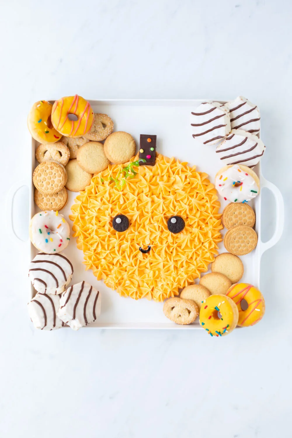 Mini donuts, cakes, and cookies on a pumpkin icing board. 