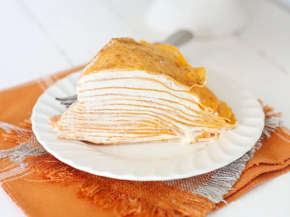 Pumpkin crepe cake with layers on a white plate on top of an orange napkin. 