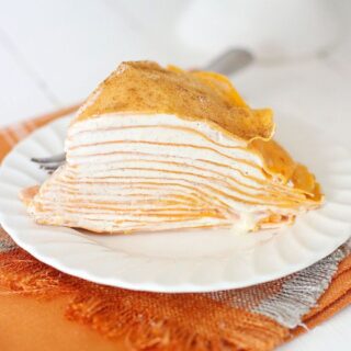 Pumpkin crepe cake with layers on a white plate on top of an orange napkin.