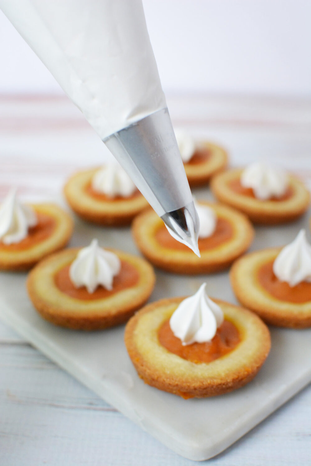 Piping whipped topping onto pumpkin pie sugar cookies. 