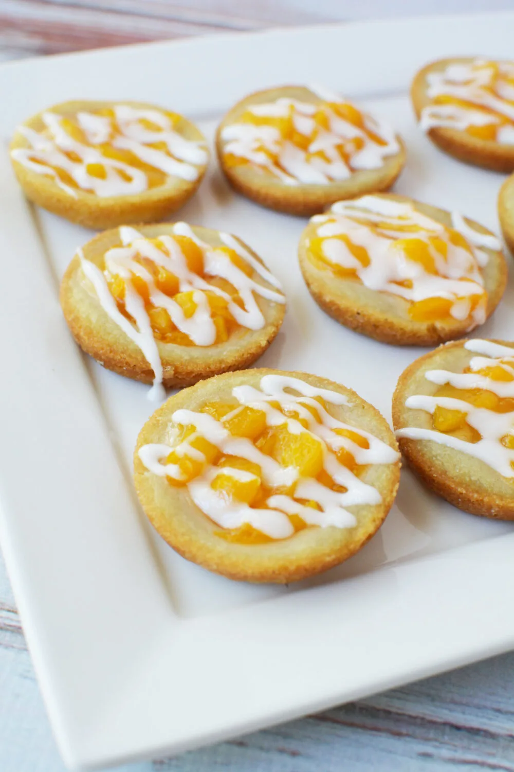 Peach pie sugar cookies with icing drizzle on a white serving tray. 