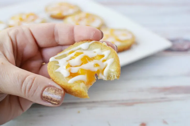 Holding a peach pie cookie with a bite missing.