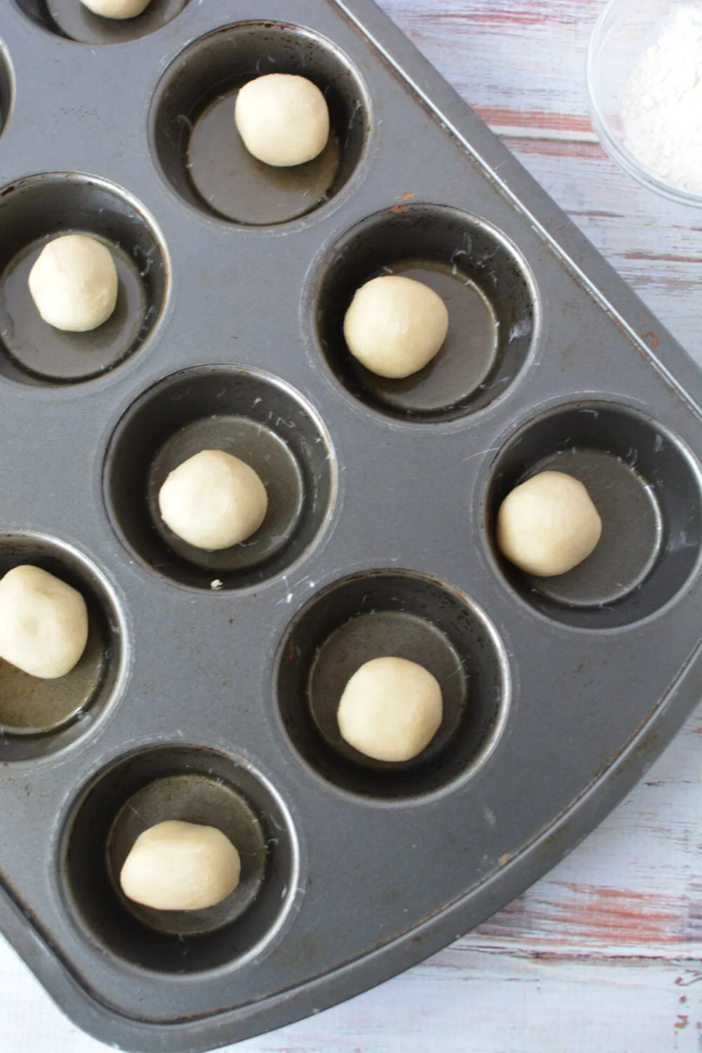 Balls of sugar cookie dough in a muffin tin. 