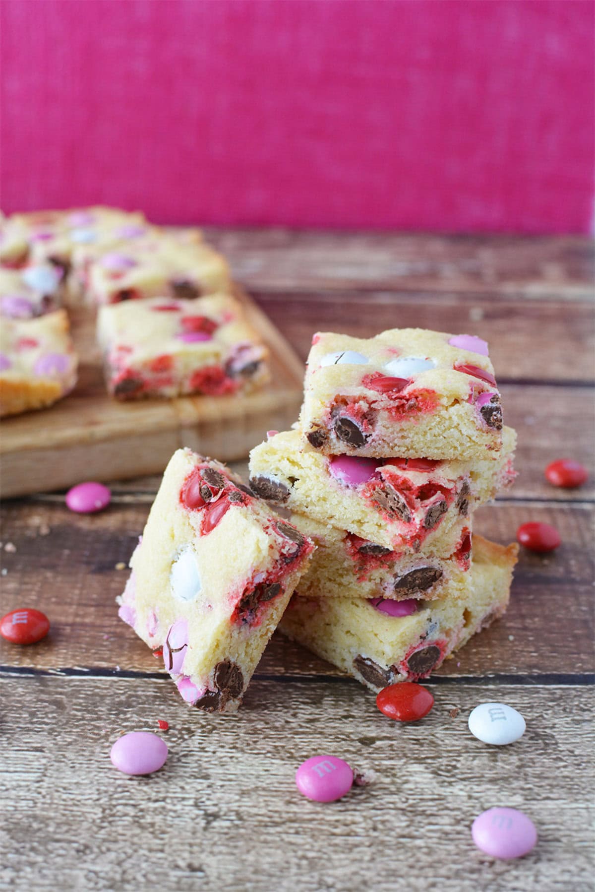 Valentine's cookie bars stacked and on a board with candies around.