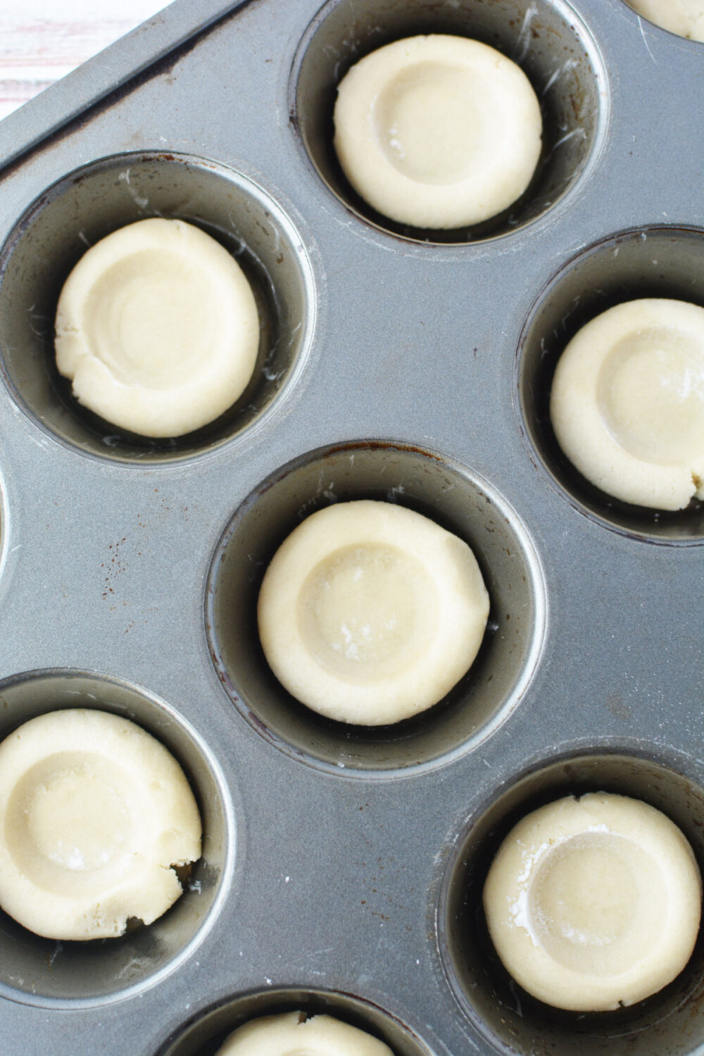 Dough shaped into mini pie crusts in baking tin. 