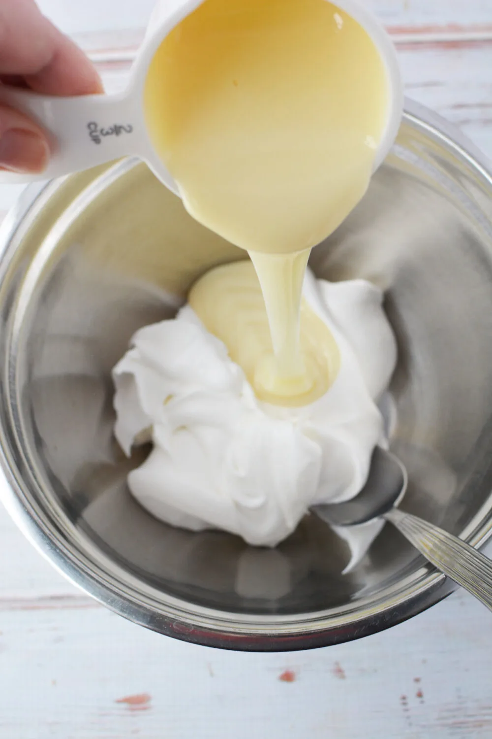 Pouring sweetened condensed milk into mixing bowl with whipped topping. 