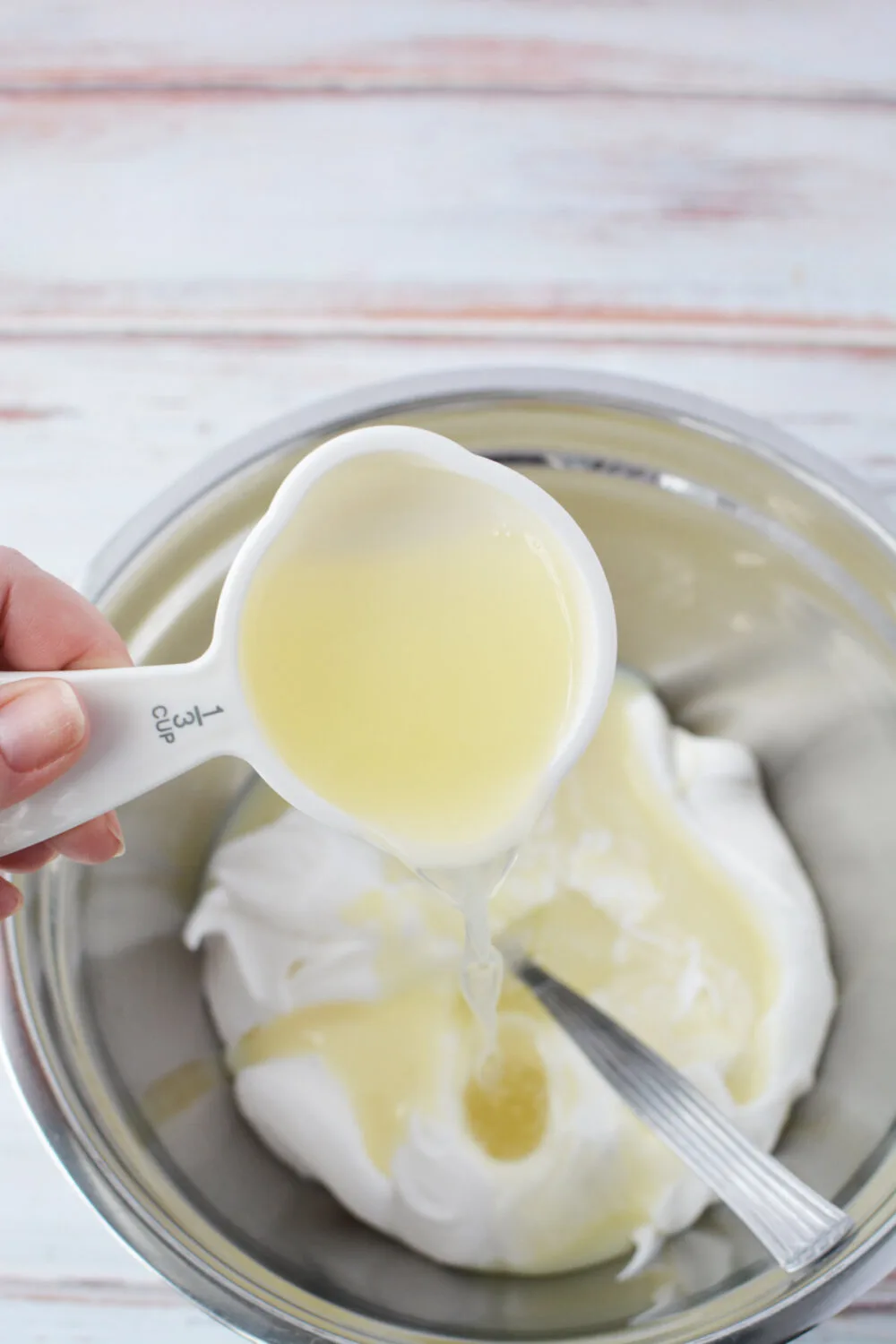 Adding lemonade to mixing bowl with whipped topping and sweetened condensed milk. 