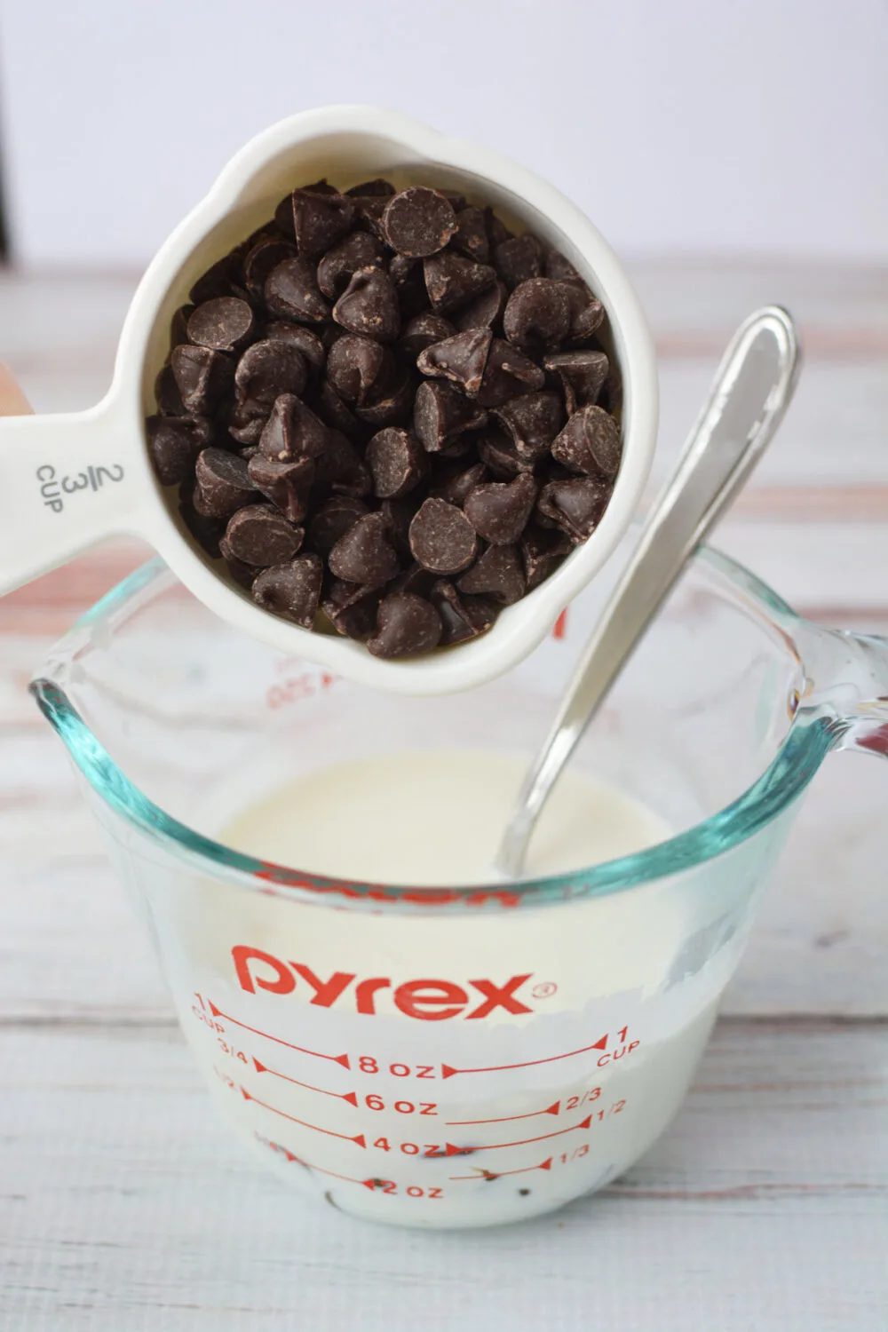 Adding chocolate chips into a measuring cup with cream.