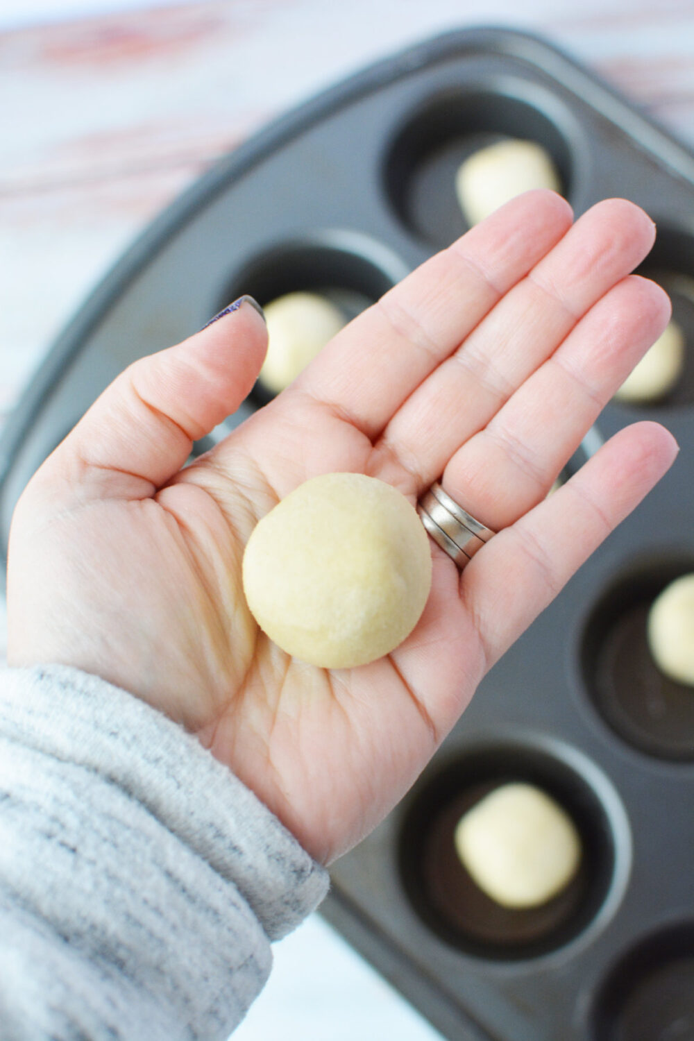 Holding a ball of sugar cookie dough above a muffin tin.