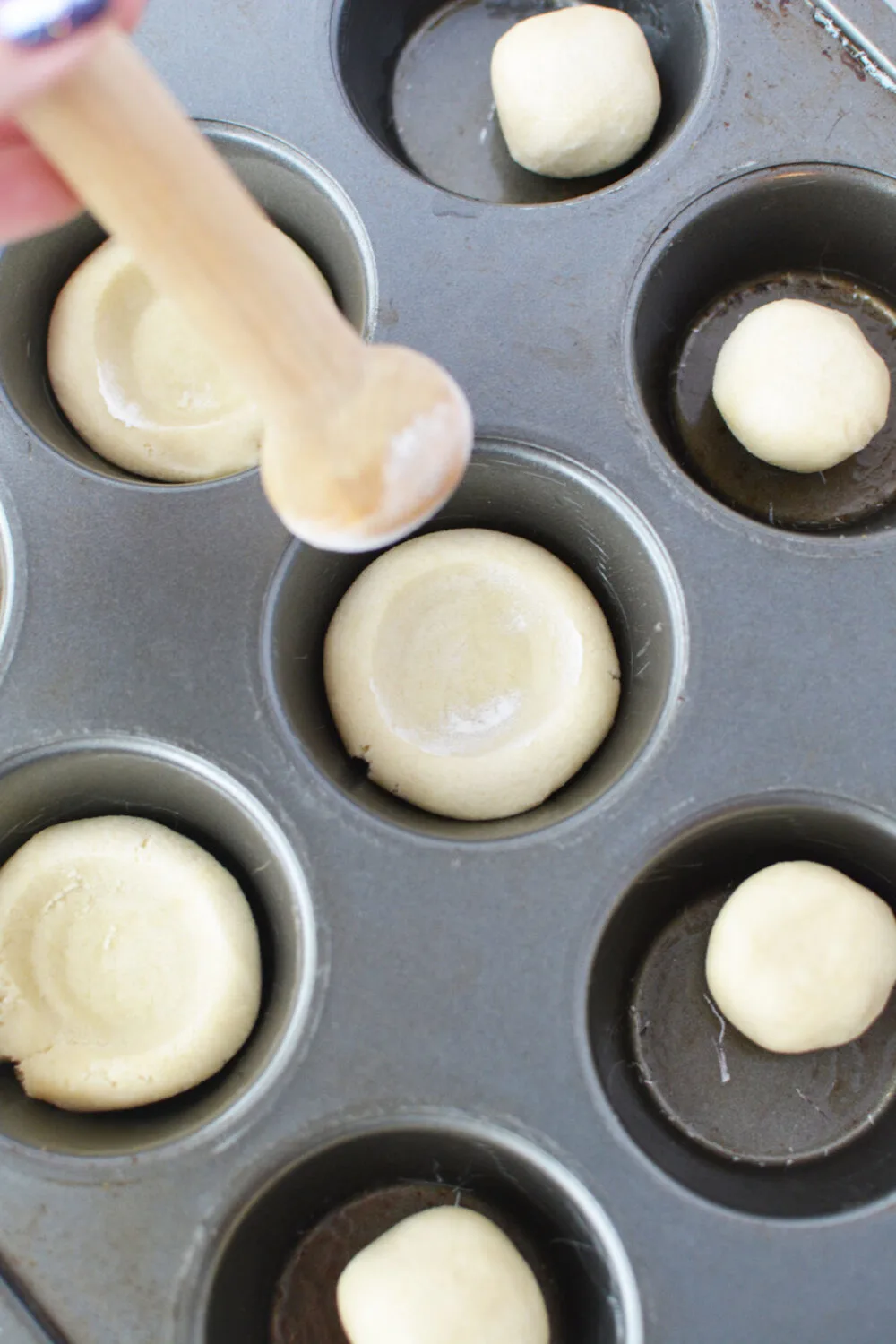 Sugar cookie dough in a muffin tin with a tart shaper being used.