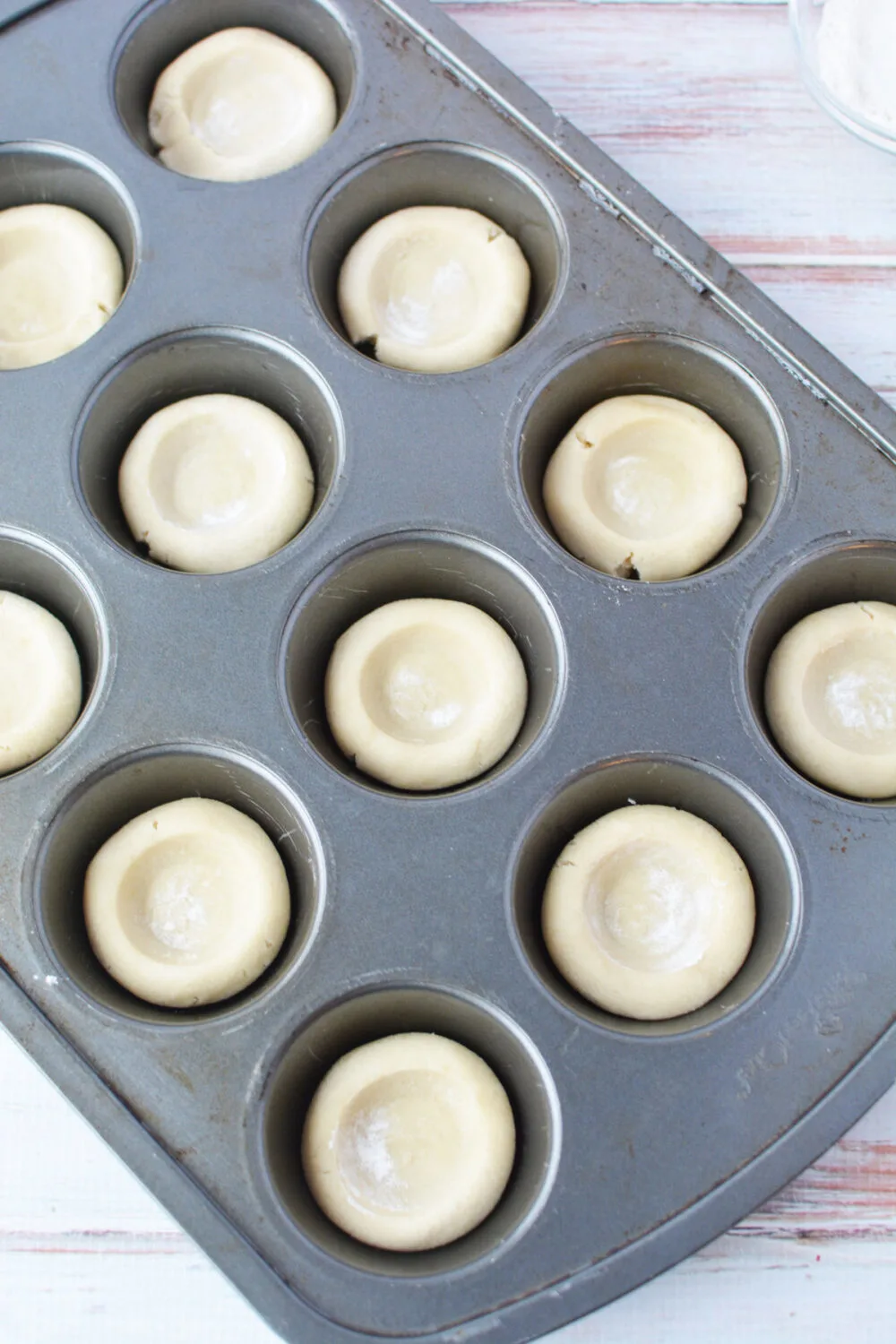 Sugar cookie dough shaped into mini pie crusts in a muffin tin.