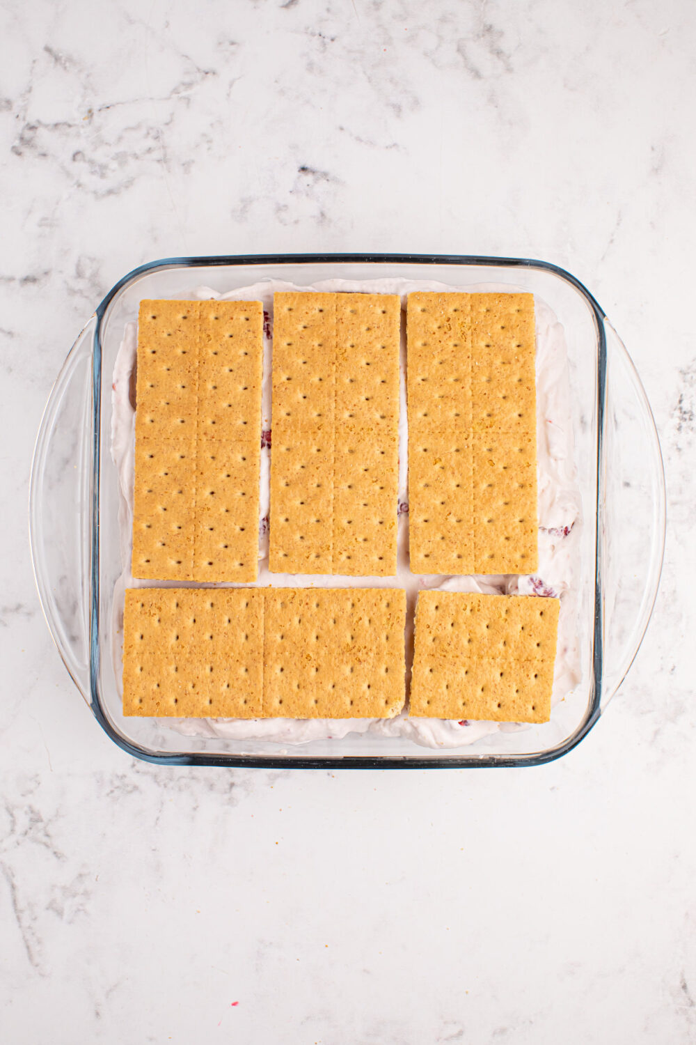 Graham crackers on top of whipped cream in a square dish. 