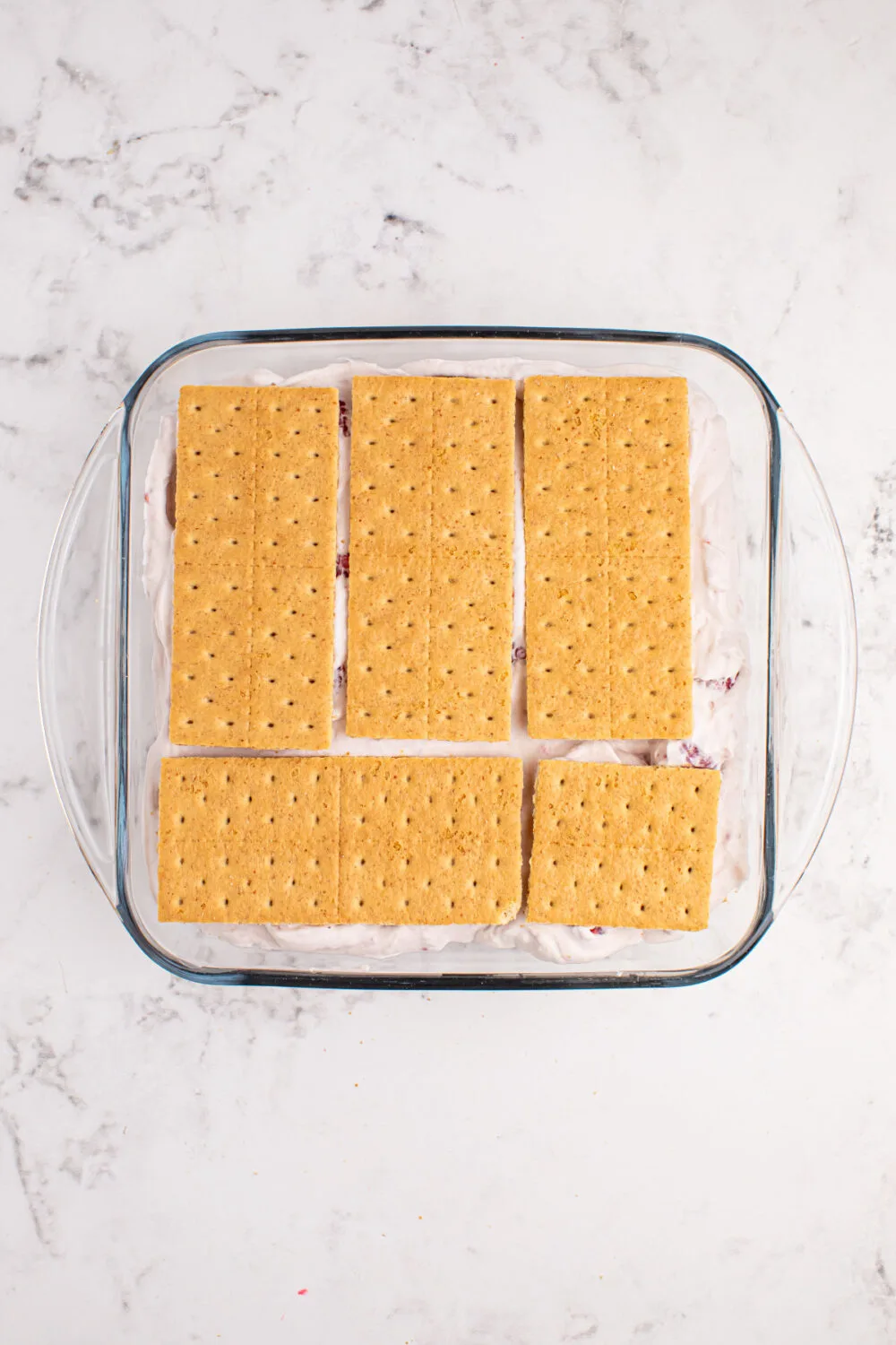 Graham crackers on top of whipped cream in a square dish. 