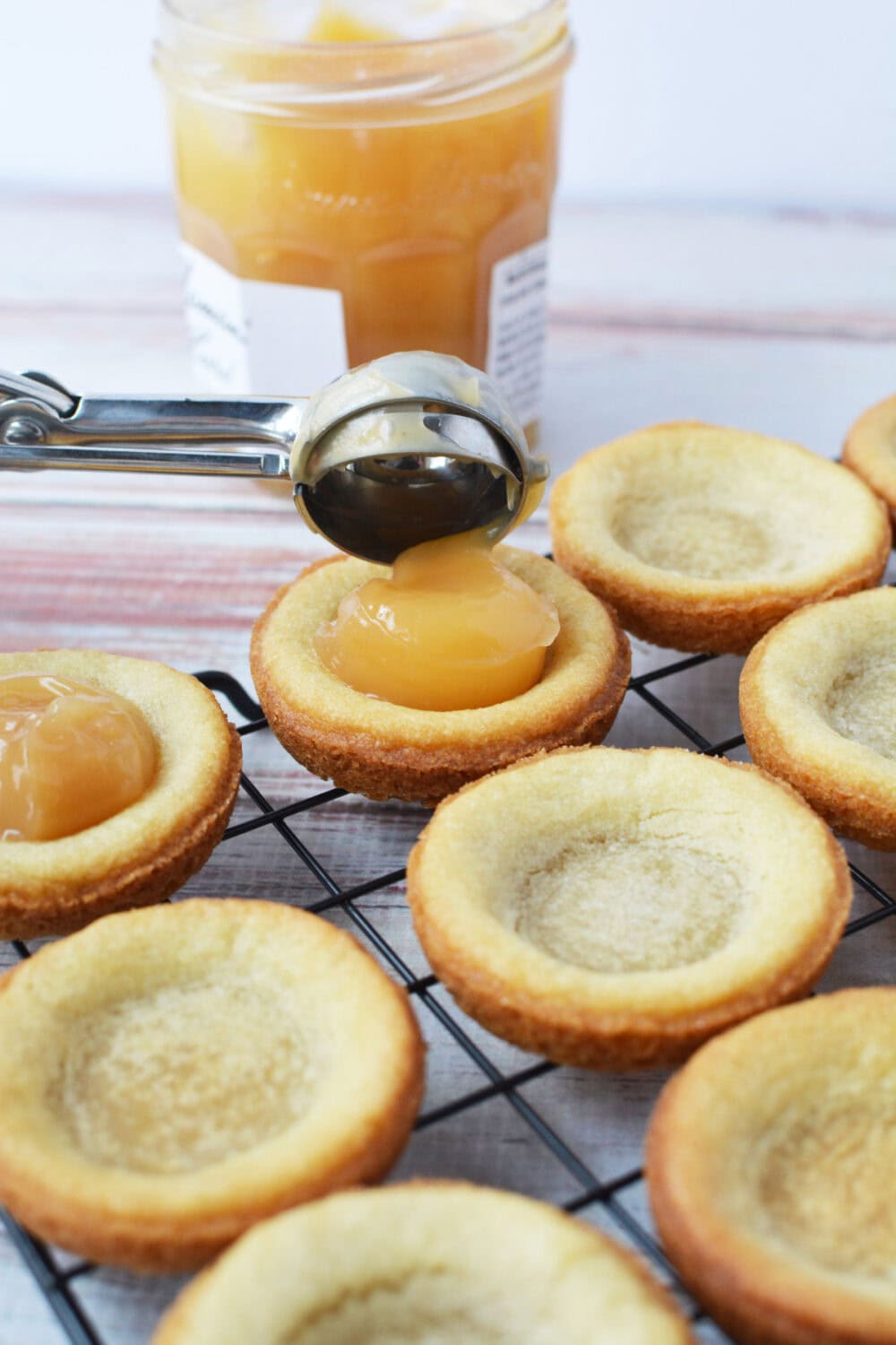 Scooping lemon curd onto baked sugar cookie crusts. 