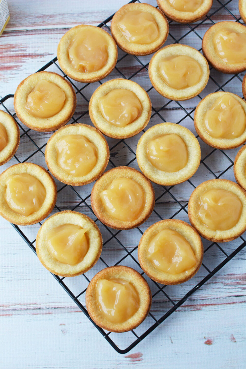 Lemon curd filled cookies on a wire rack. 