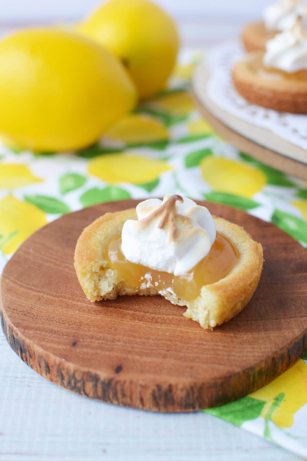 Lemon meringue pie cookies with a bite missing sitting on a wood coaster. 