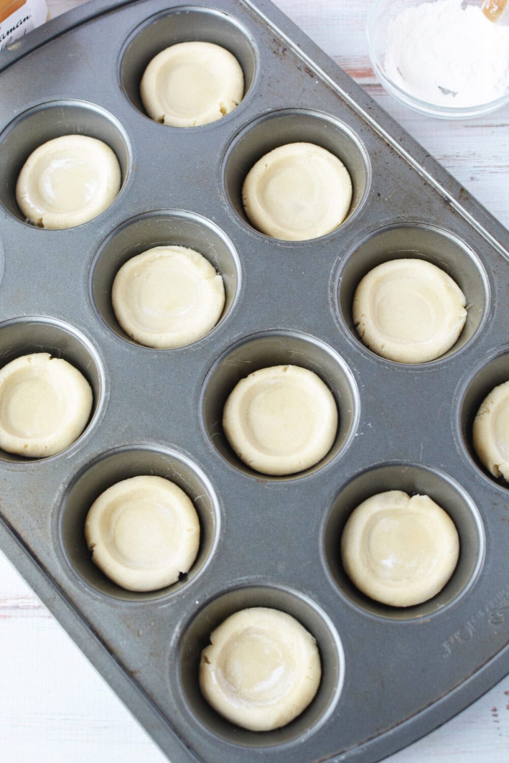 Sugar cookie crusts ready in a muffin tin. 