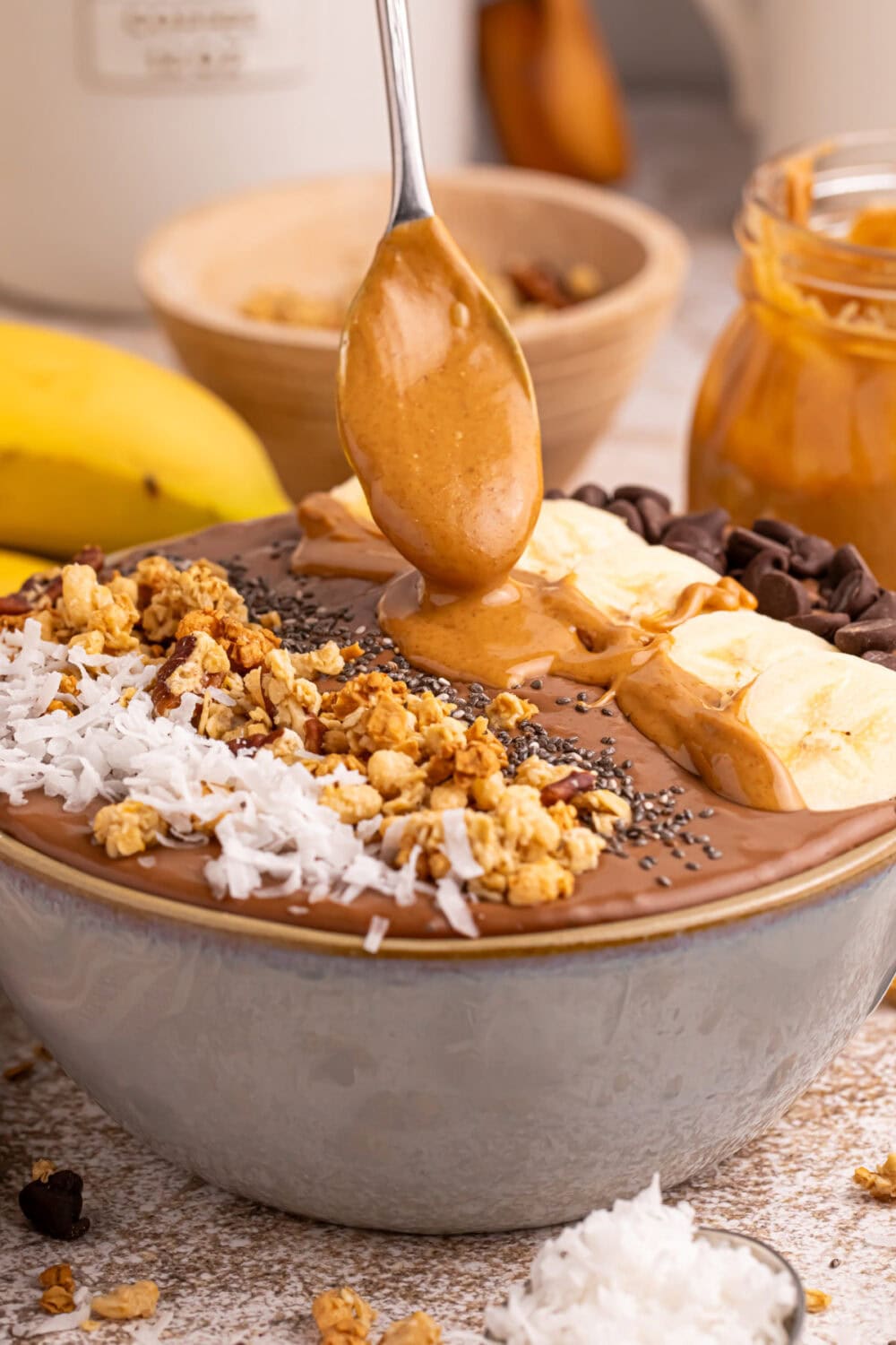 Spooning peanut butter onto a chocolate smoothie bowl. 