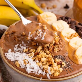 Spoon lifted out of a chocolate peanut butter smoothie bowl.