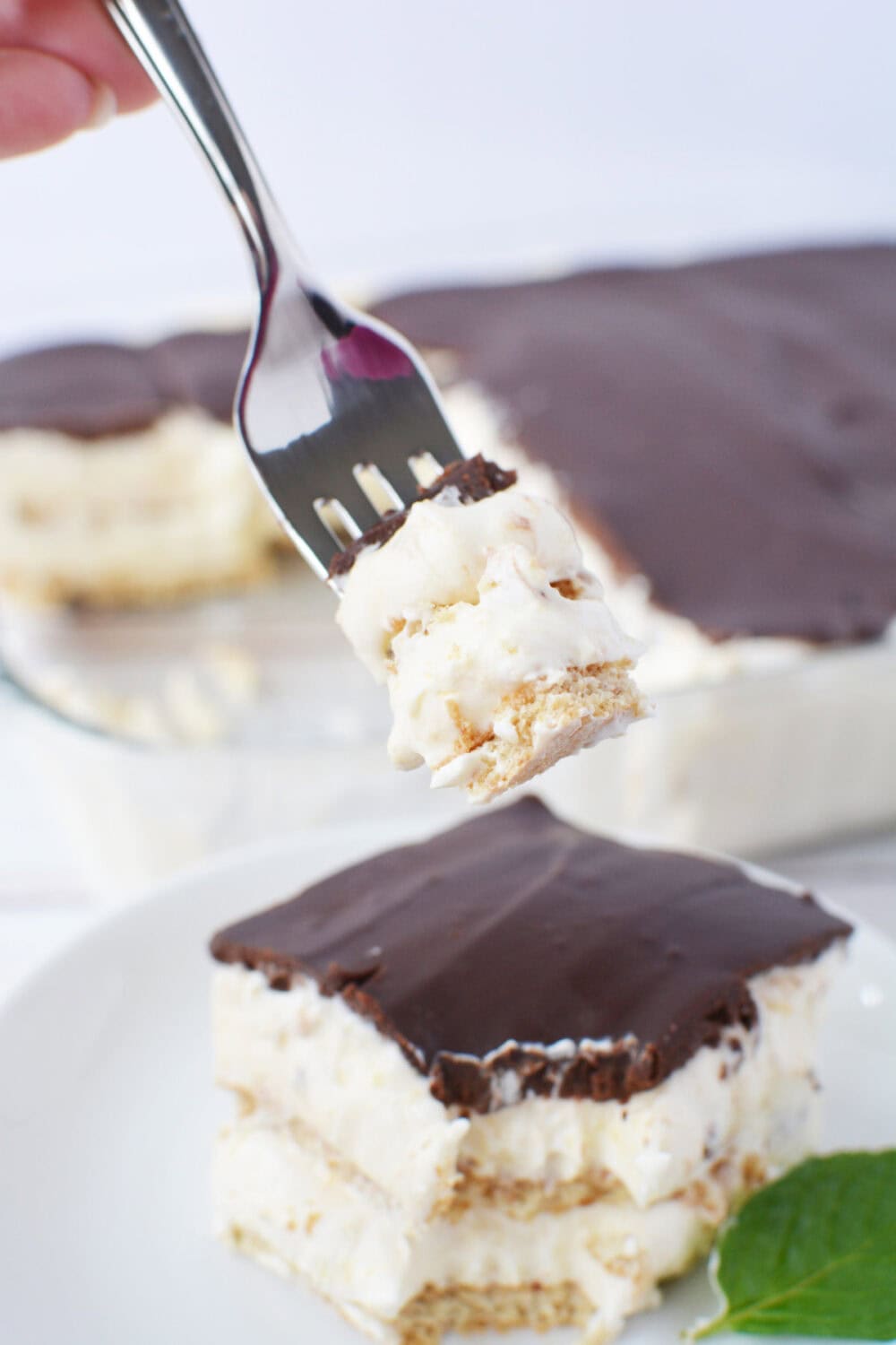 Fork with eclair cake over the slice on a plate. 