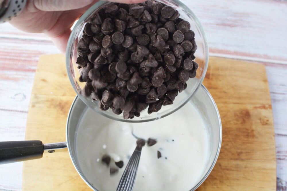 Adding chocolate chips to cream in a saucepan.