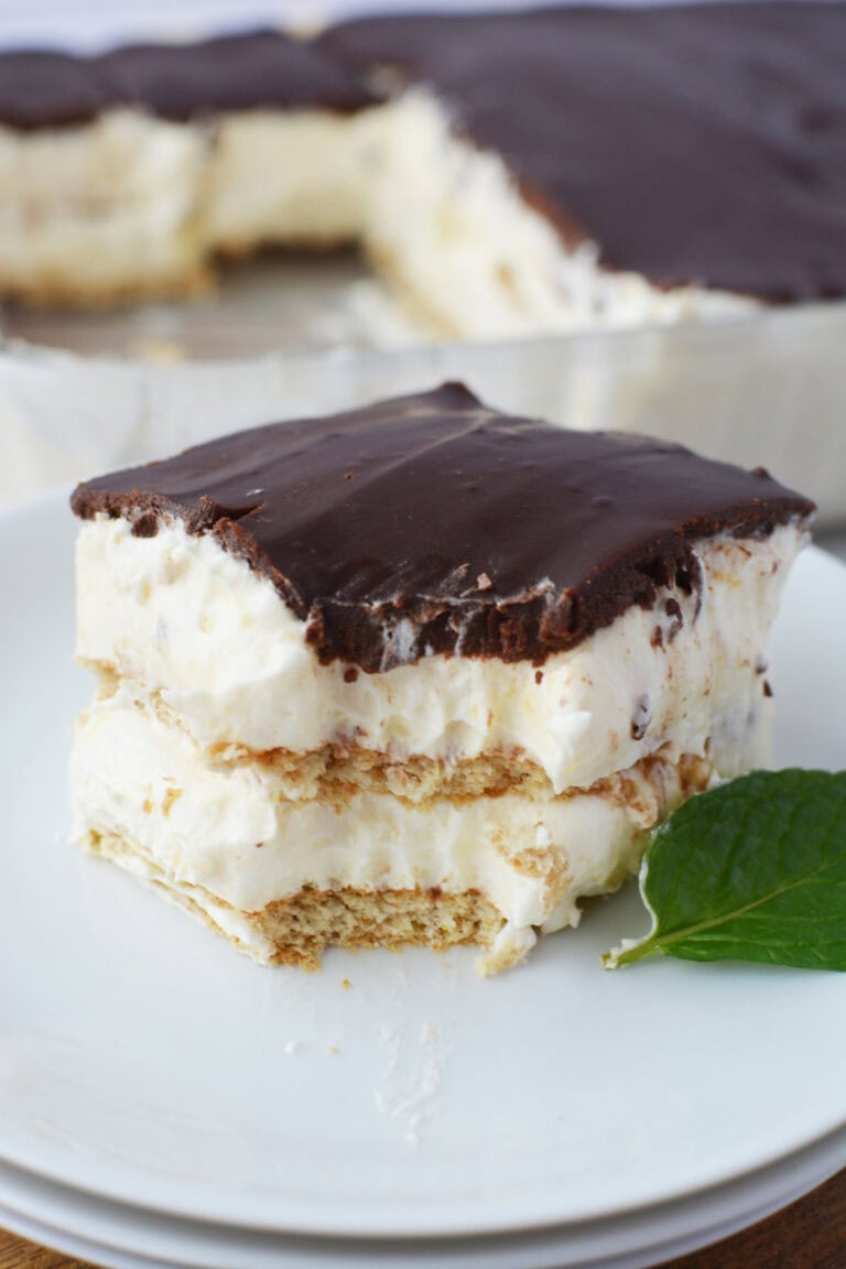 Slice of chocolate eclair cake on a white plate next to a mint leaf.