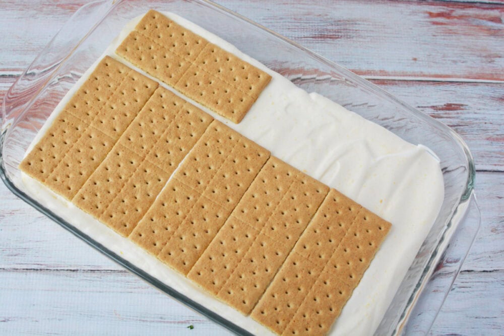 Graham crackers on top of pudding mixture in a clear pan.