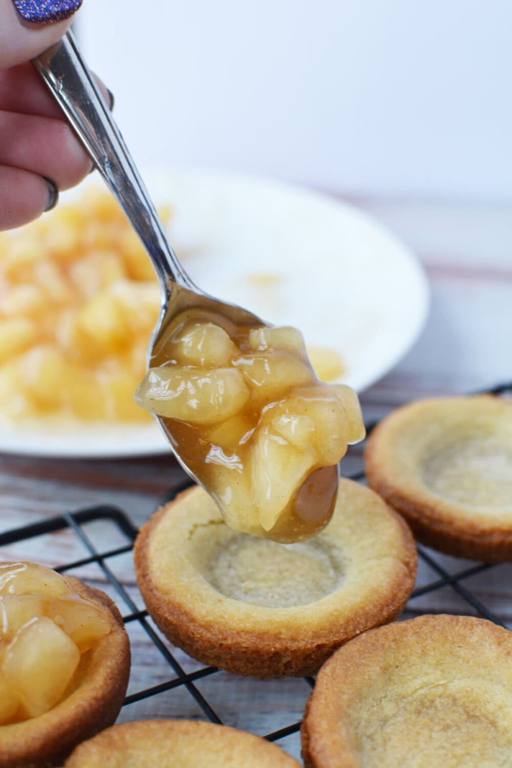 Spooning apple pie filling into cookie crusts. 