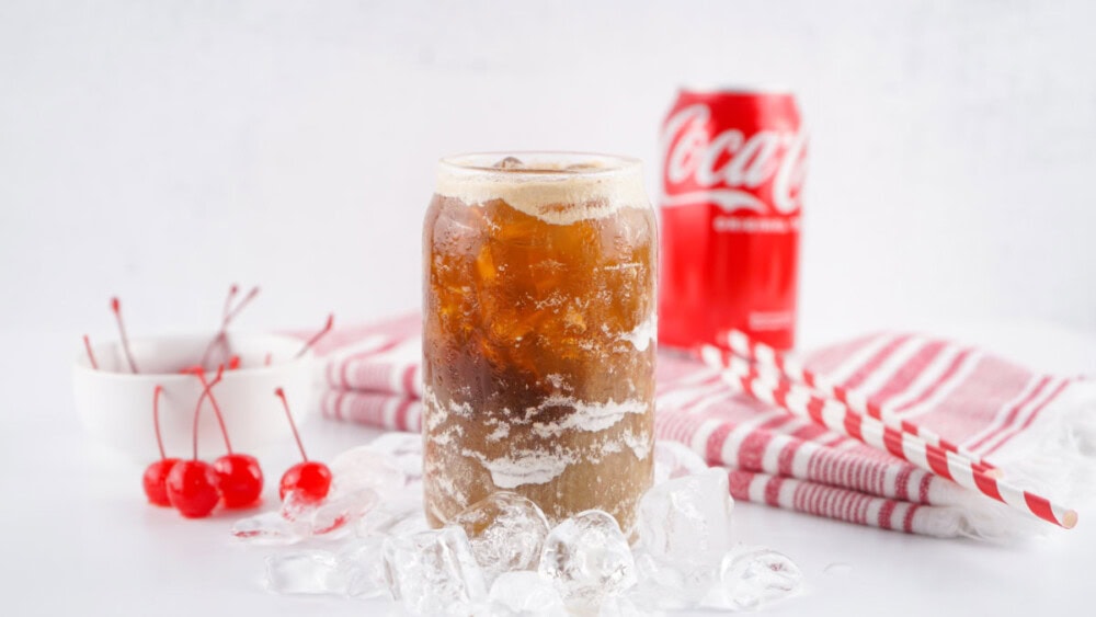 Can of Coca-cola classic, cherries, ice, straws, and glass of Fluffy Coke. 