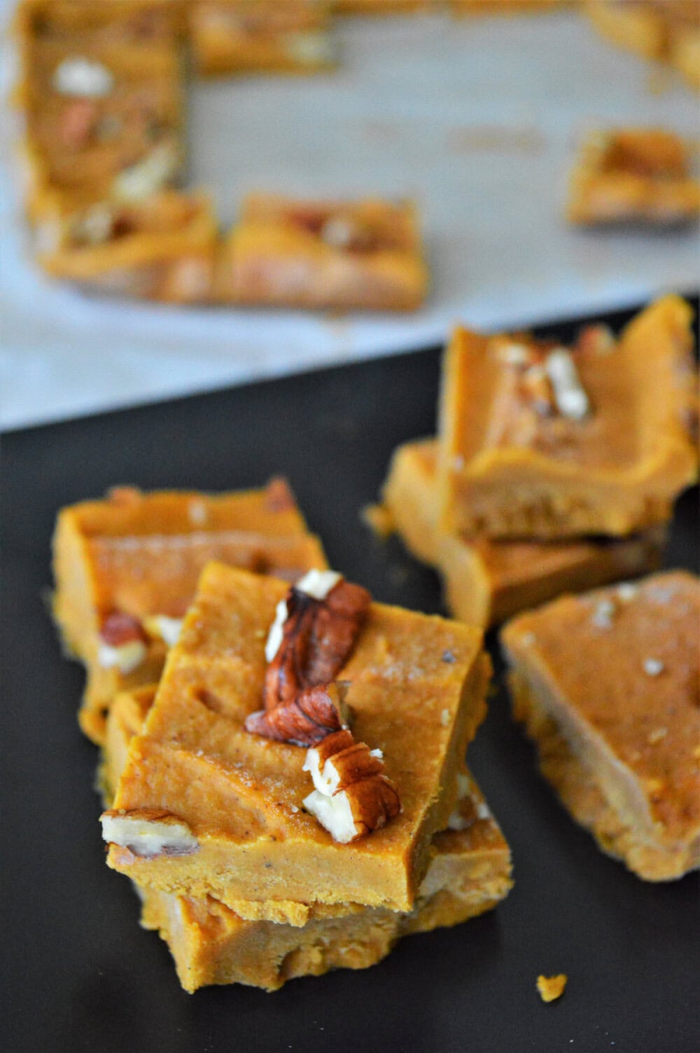 Sliced pumpkin fudge topped with pecans on a board. 