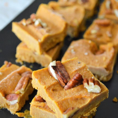 Peanut butter pumpkin fudge topped with pecans stacked on a board.