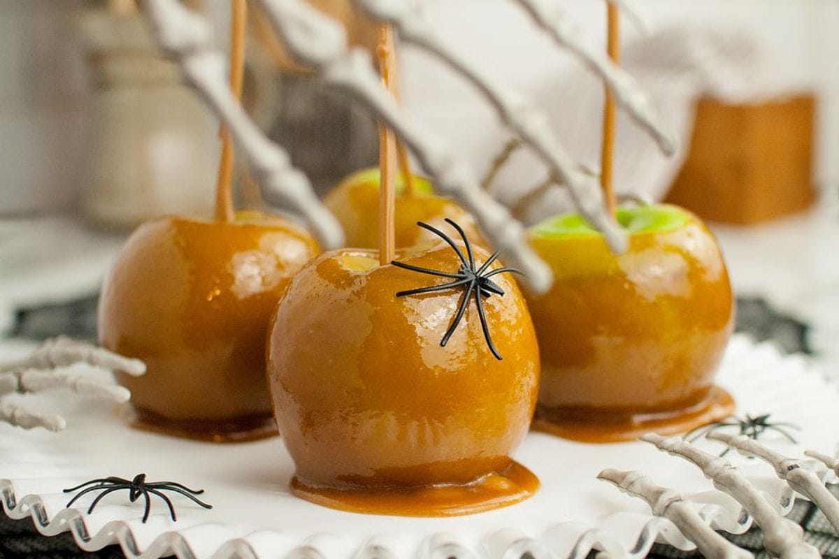 Caramel apples on a plate with spiders and Halloween decor.