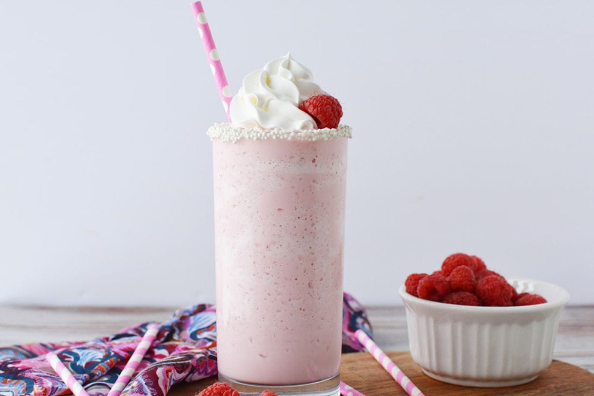 Cotton candy frappe next to a bowl of raspberries. 