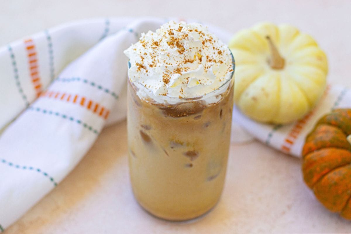 Iced pumpkin latte in a glass topped with whipped cream.