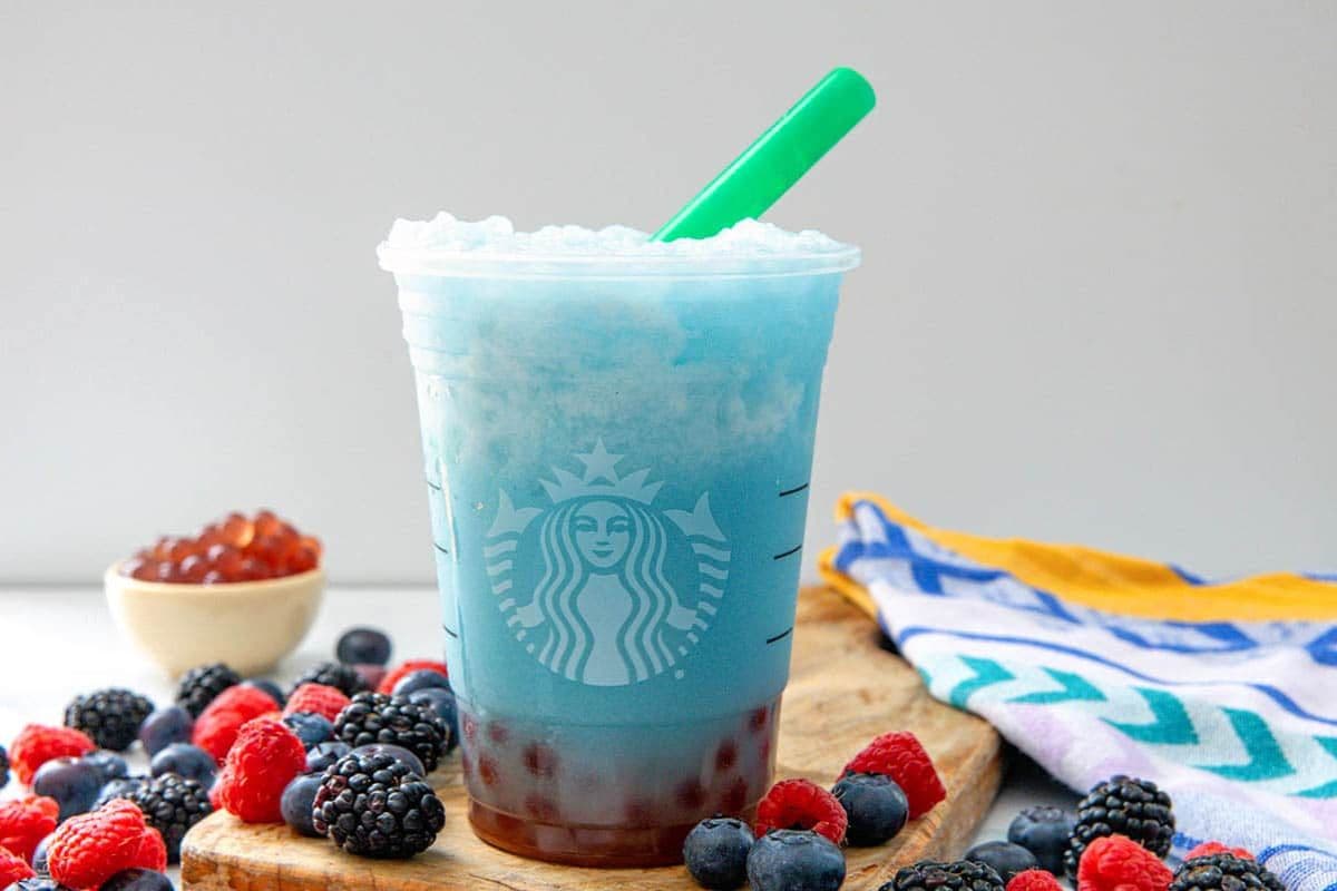 Icy blue drink in a cup surrounded by fruit. 