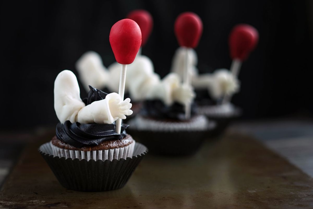 Clown arm holding a red balloon on a cupcake. 