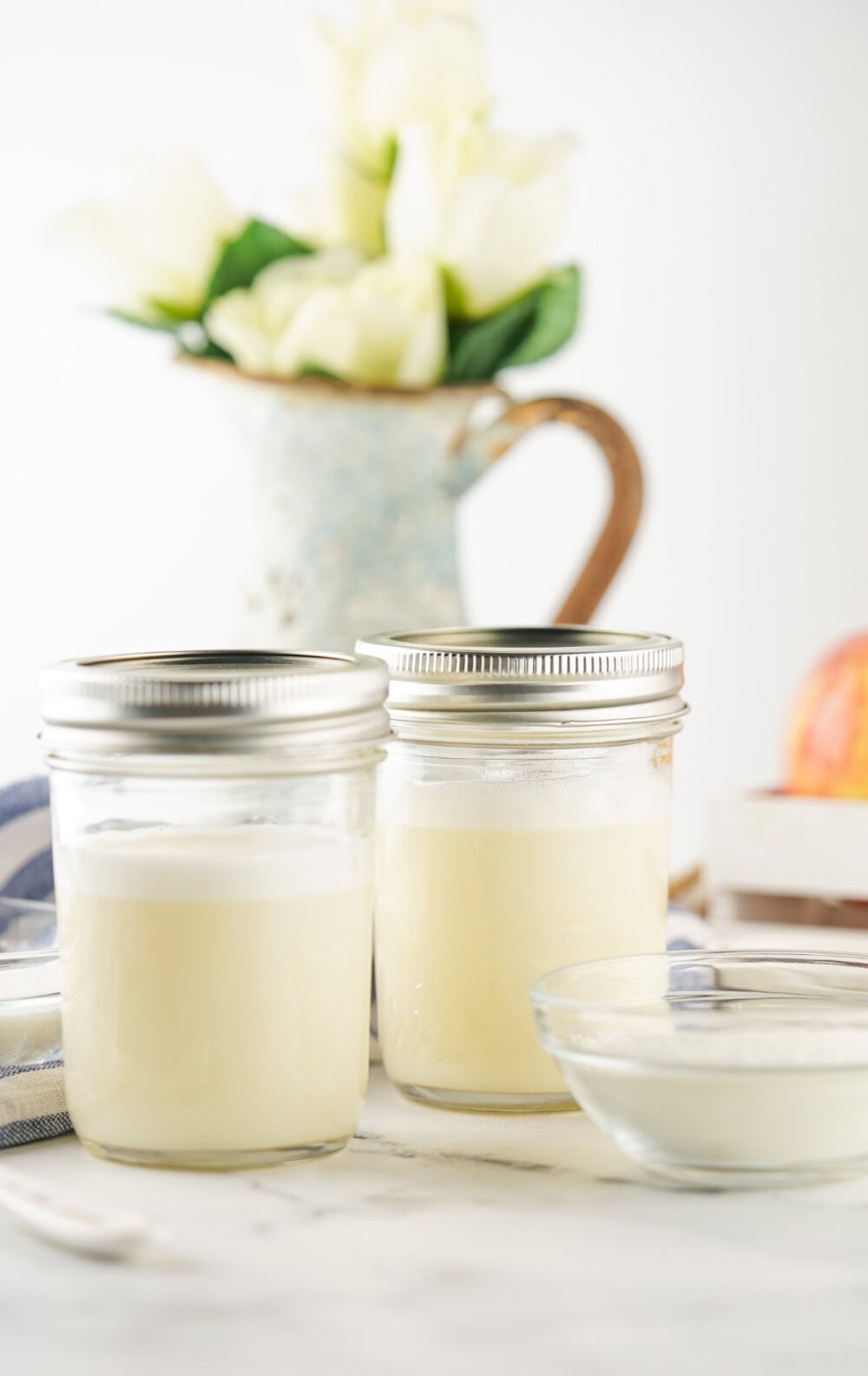 Two jars of condensed milk next to flowers. 