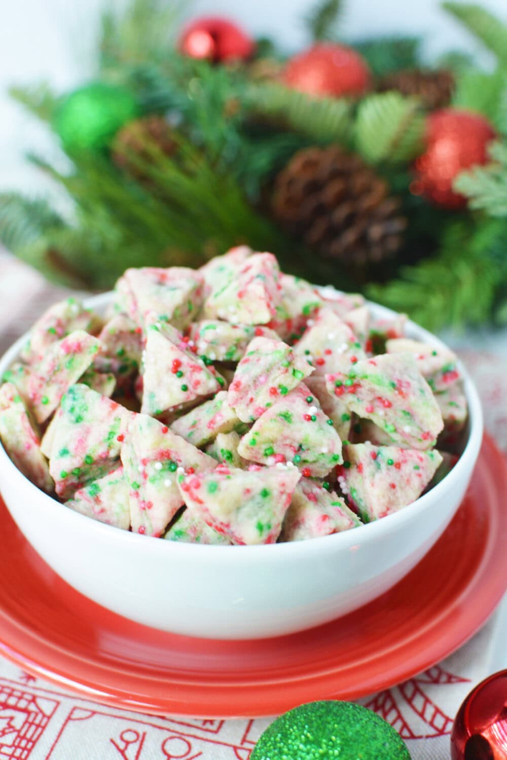 Mini holiday shortbread bites in a white bowl with Christmas decor on the table. 