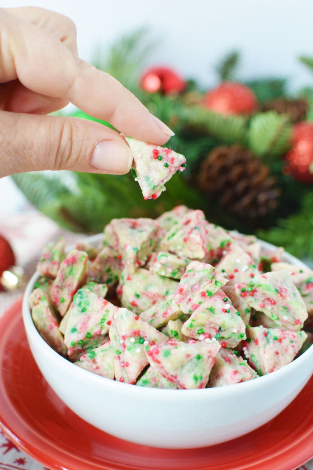 Holding an elf bite mini cookie over the bowl of shortbread bites. 