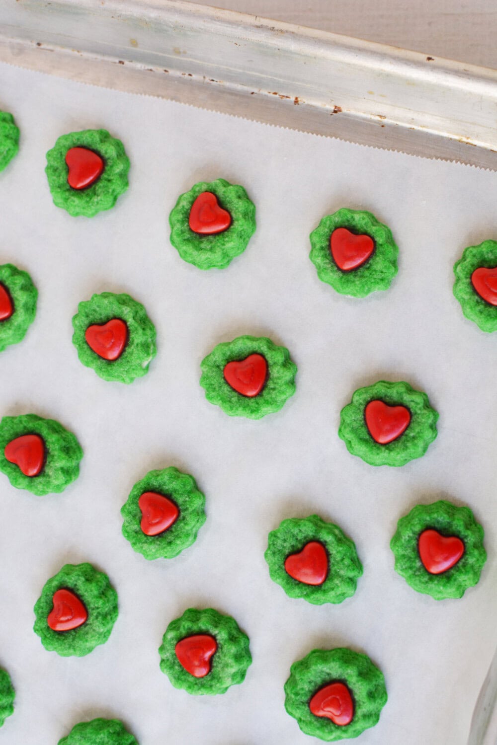 Green cookies with red hearts on a baking sheet. 