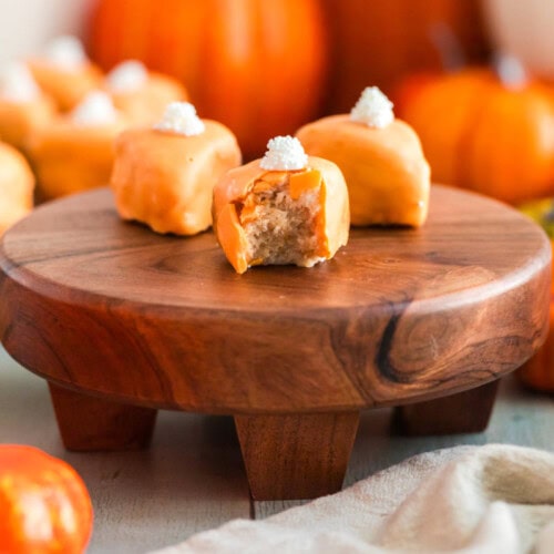 Pumpkin pie slice cake bites on a board and one has a bite taken out of it.