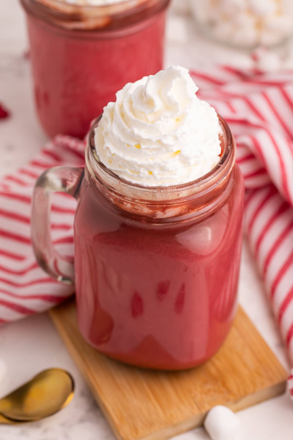 Jar of red chocolate drink topped with whipped cream. 