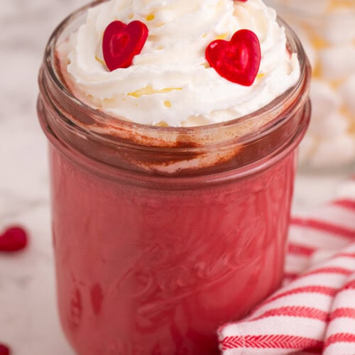 Red hot chocolate in a jar topped with whipped cream and heart candies.