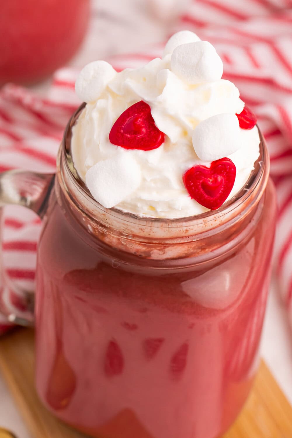 Glass jar with red hot chocolate with a whipped cream and sprinkle topping. 