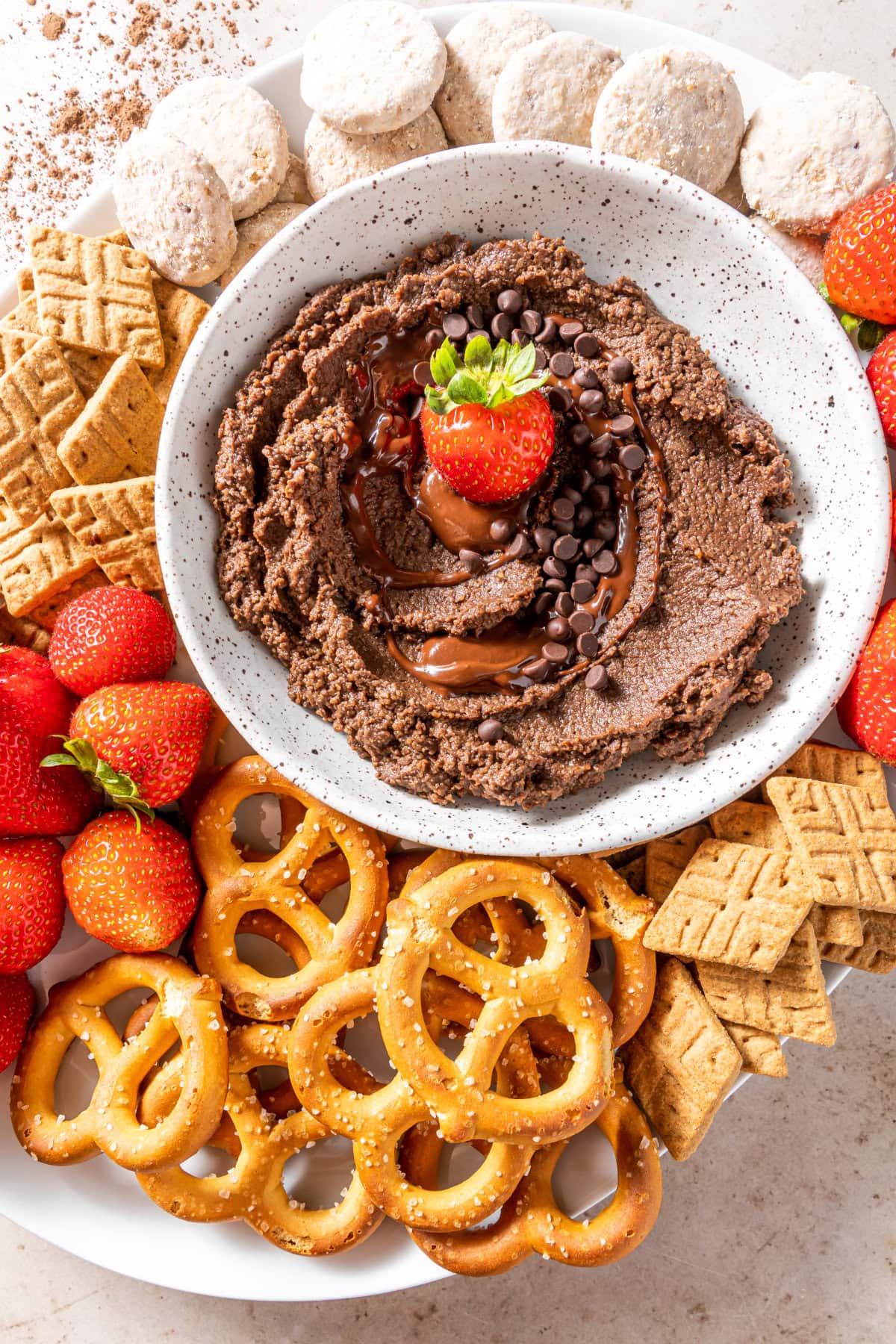 Bowl of chocolate hummus surrounded by pretzels, strawberries, and tiny crackers.