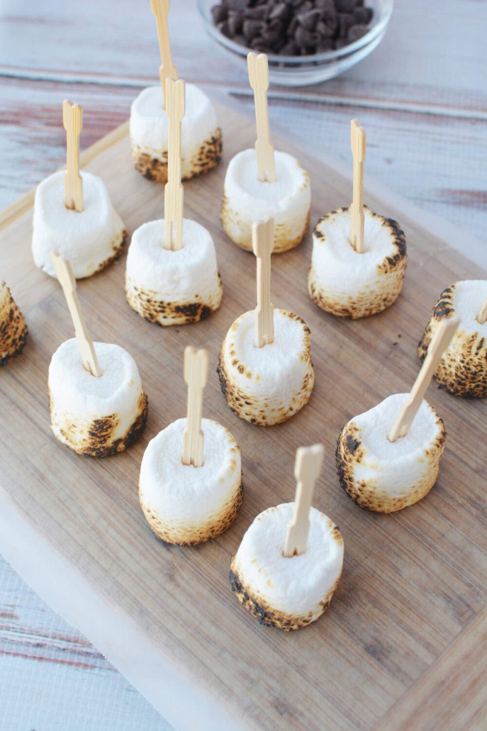 Toasted marshmallows on skewers on a board.