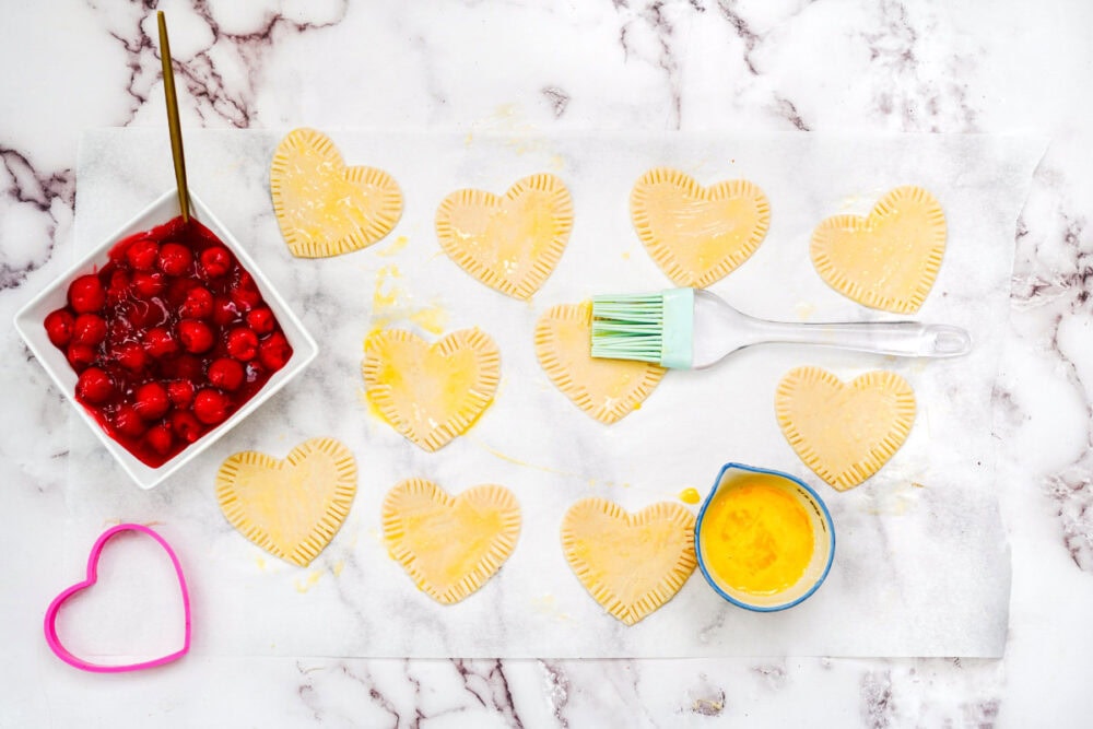 Brushing heart pastries with egg.